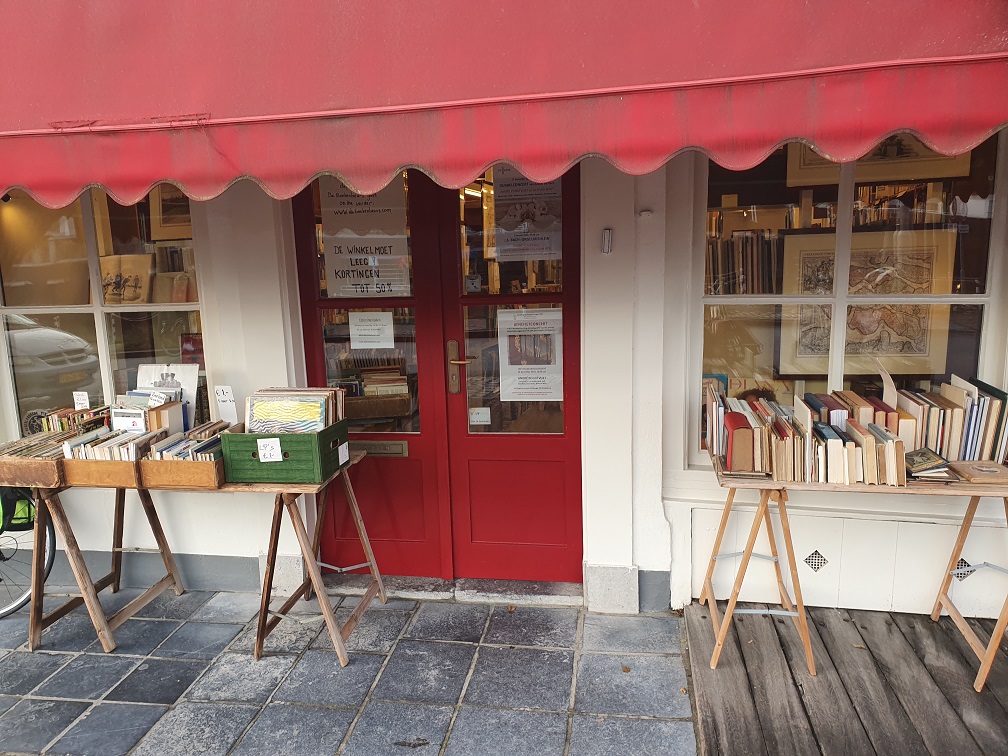 Front view of a bookstore with books stalled out in front of the shop window sheltered by a canopy above them