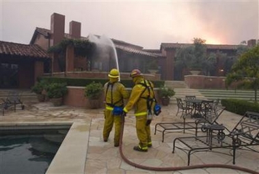 Firefighters water down the roof of a house to douse the embers from the approaching flames of a fast moving wildfire in Rancho Santa Fe, California, October 22, 2007