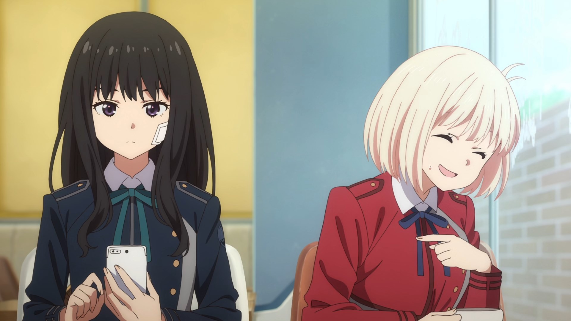 A calm black haired school girl is looking at her mobile while a short haired, blonde girl is laughing awkwardly and pointing at her
